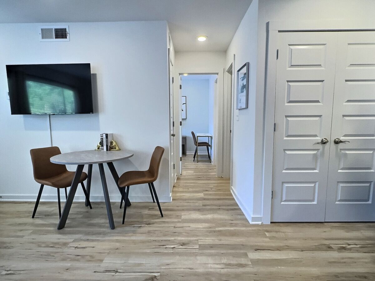 A modern interior with a dining area, a TV mounted on the wall, and a hallway leading to another room.