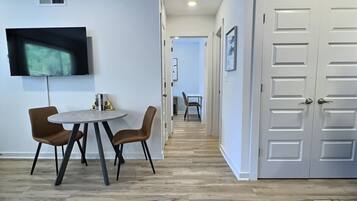 A modern interior with a dining area, a TV mounted on the wall, and a hallway leading to another room.