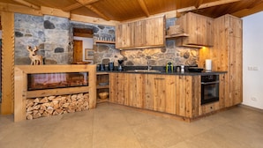A rustic kitchen with wooden cabinets, a stone wall, and a built-in fireplace.