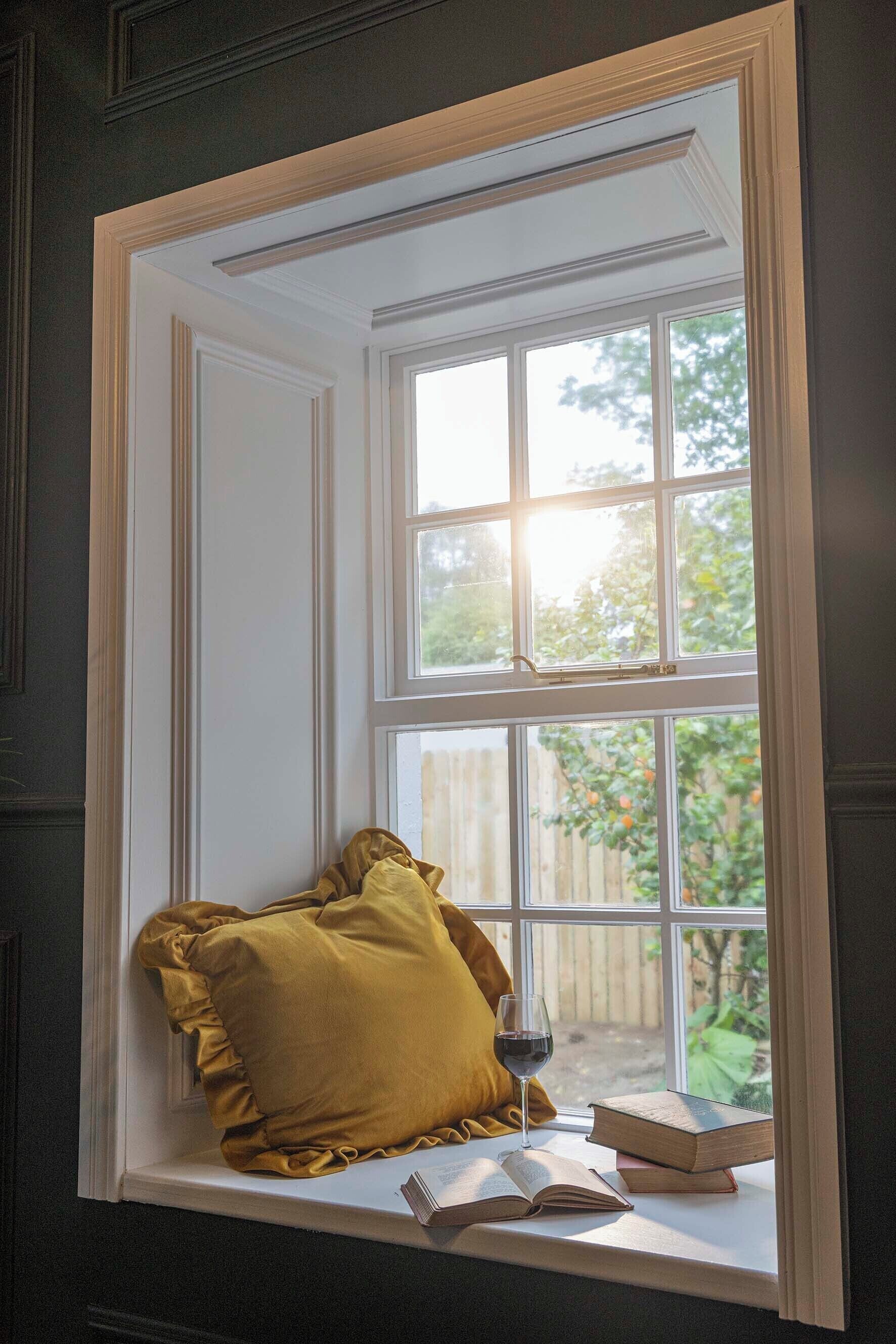 A window seat with a cushion, a glass of wine, and books.