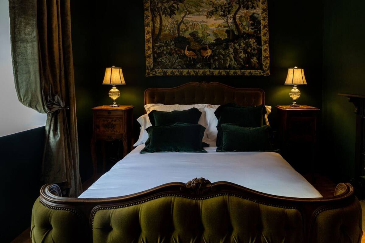 Een slaapkamer met een groot bed, twee nachtkastjes met lampen, een schilderij aan de muur en een kamerplant.