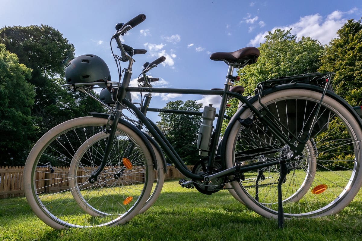Een stilstaande fiets met helm, waterfles en zadel in een grasrijk buitengebied.