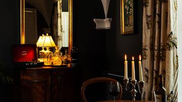 Une pièce faiblement éclairée, avec un grand miroir, une table sur laquelle se trouvent une lampe, des bougies et une bouteille.