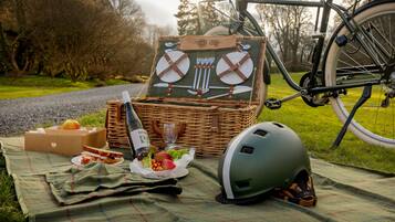 A picnic setup with a wicker basket, a bicycle, and a helmet on a blanket.