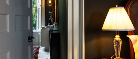 A hallway with a white door, a sink, a mirror, and a lamp.