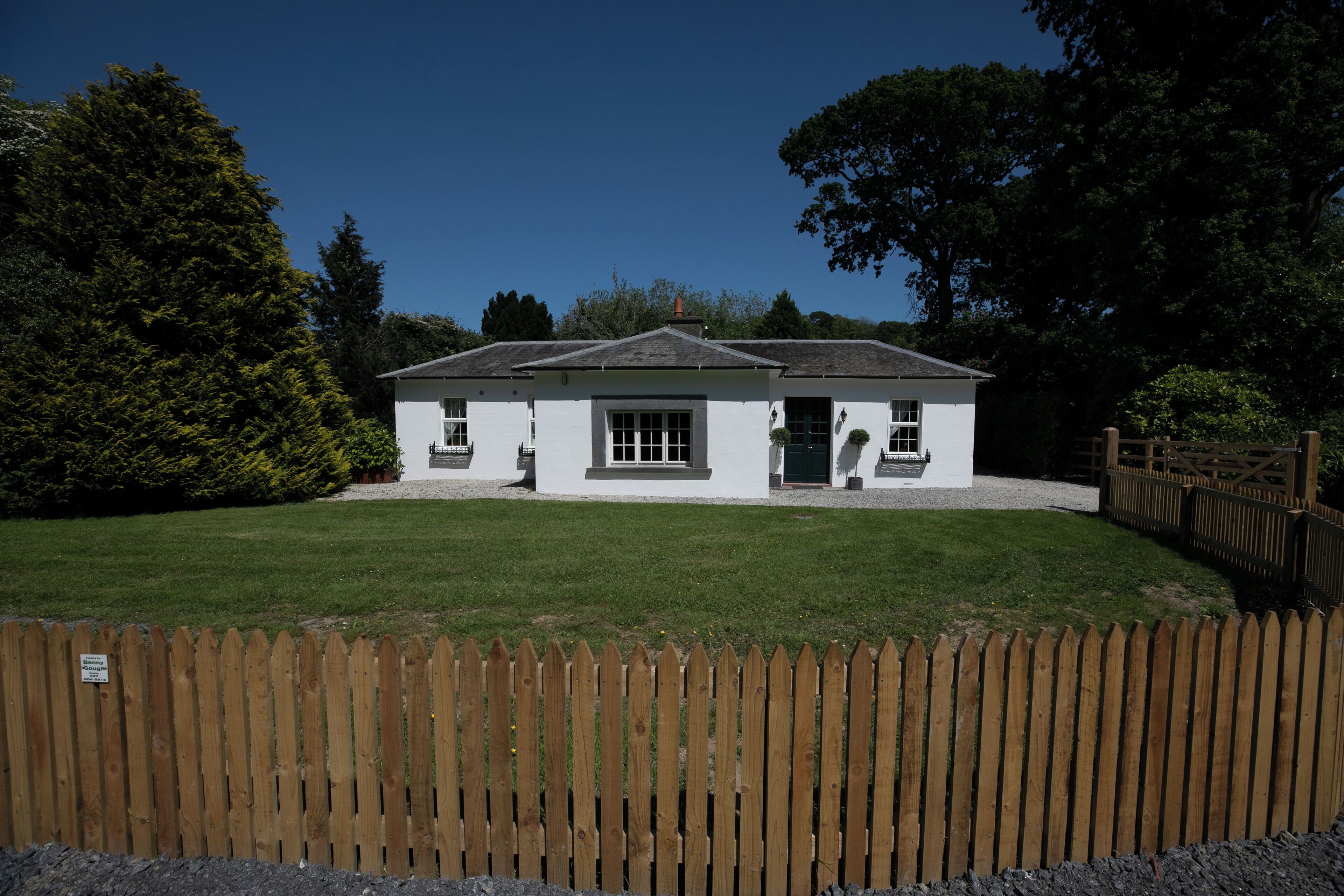 A white building with a sloped roof, a wooden fence in the foreground, and a well-maintained lawn.