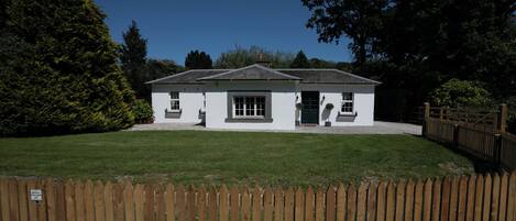 A white building with a sloped roof, a wooden fence in the foreground, and a well-maintained lawn.