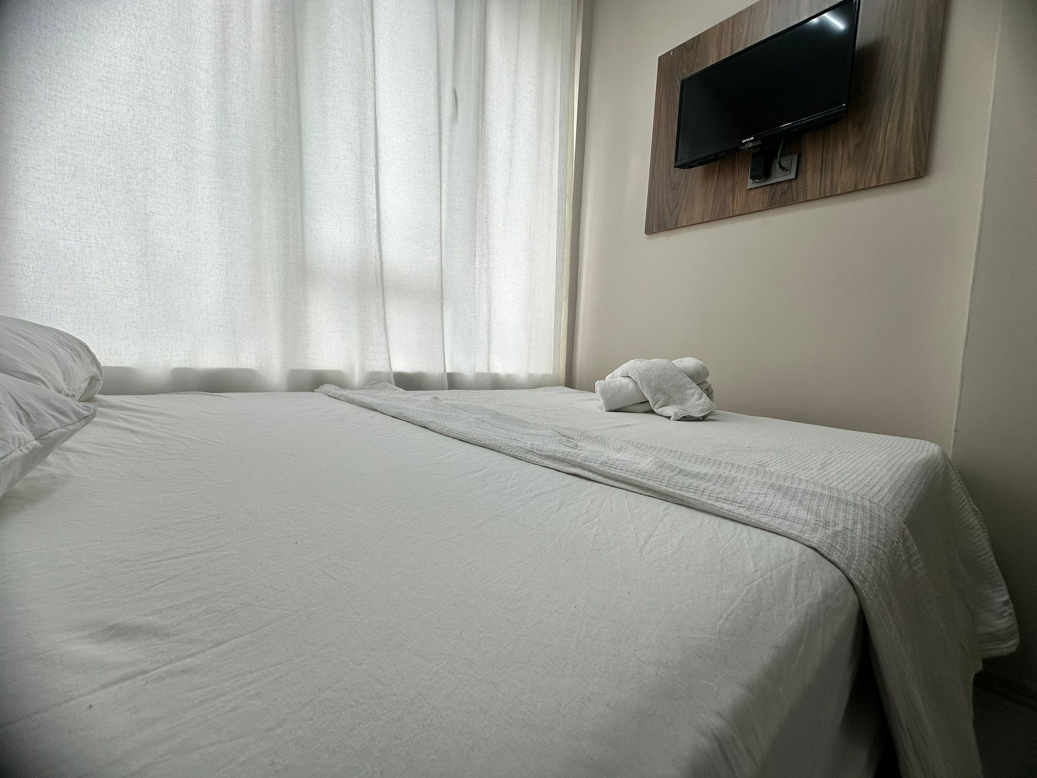 Ein Hotelzimmer mit Bett, Wandfernseher und einem Fenster mit Vorhängen.