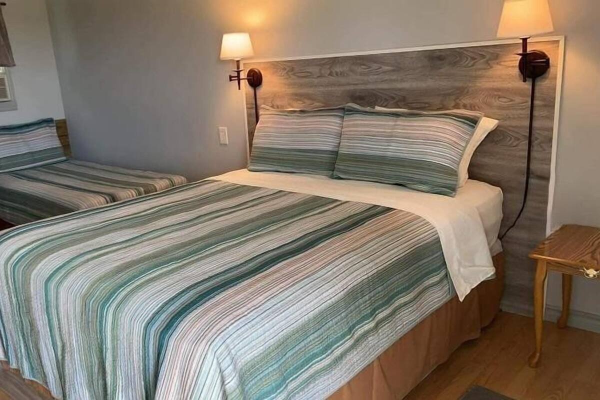 Une chambre avec deux lits, une tête de lit en bois, des lampes de chevet et une petite table.