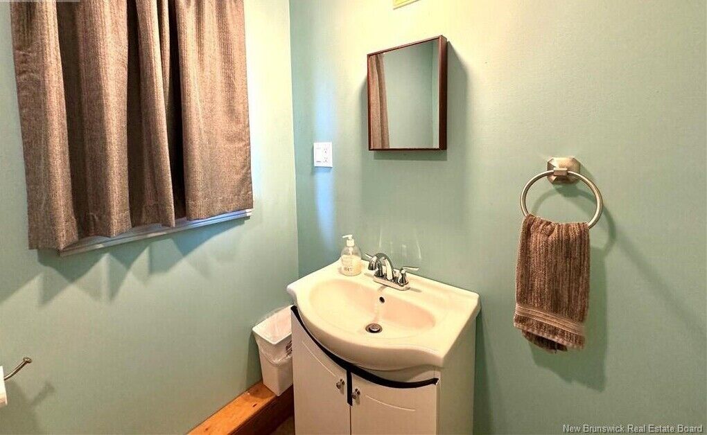A bathroom with a sink, mirror, towel rack, and window with curtains.