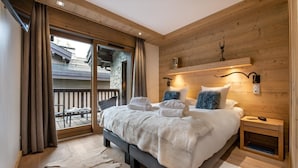 Une chambre avec un grand lit, des murs en bois, un balcon avec vue et une petite table de chevet avec une lampe.