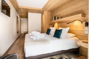 A hotel room with a wooden ceiling, a bed with white linens and teal pillows, a bedside table with a lamp, and a small rug. - Wifi, 150m from resort center, 2nd floor, view mountain, sauna, balcony, fireplace or stove, parking (Courchevel)