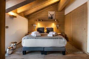 A cozy bedroom with a large bed, wooden beams, a framed deer picture, and a small bedside table with a lamp. - Wifi, 150m from ski slopes, 3rd floor, view mountain, sauna, balcony, fireplace or stove, parking (Courchevel)
