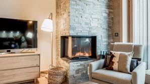 Ein gemütliches Wohnzimmer mit Kamin aus Stein, einem Flachbildfernseher, einem bequemen Sessel und einem Korbwannenmöbel.
