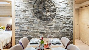 A dining area with a stone wall, a large clock, and a table set for two with wine glasses and plates. - Wifi, 150m from resort center, 3rd floor, sauna, balcony, parking, tv, 64m², Courchevel (Courchevel)