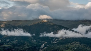 Un paisaje montañoso con un pico destacado, valles boscosos y una capa de nubes a los pies de la montaña.