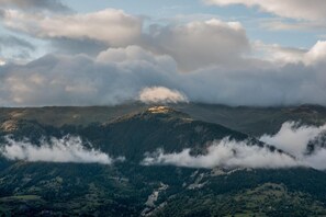A mountainous landscape with a prominent peak, forested valleys, and a layer of clouds at the mountain base.