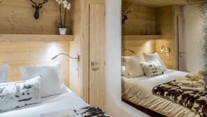 A room with wooden walls, a bed with white bedding, and a large mirror reflecting the room. - Wifi, 150m from resort center, 3rd floor, sauna, balcony, parking, tv, 64m², Courchevel (Courchevel)