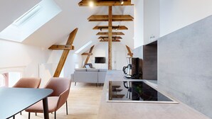 A modern kitchen with a glass-top island, wooden beams, and a flat-screen TV.