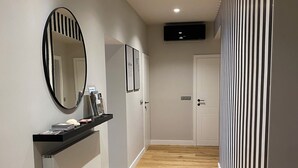 Un couloir doté d’un plancher en bois, d’un miroir à cadre noir, d’un petit tabouret noir et d’une porte blanche au fond.