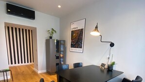Un espace repas moderne avec une table et des chaises noires, une affiche au mur et un meuble orné de plantes.