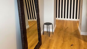 Un couloir avec un grand miroir, un petit tabouret et un climatiseur noir fixé au mur.
