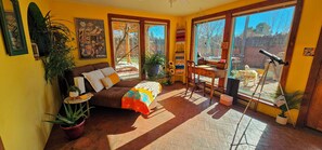 Una habitación con una cama, un escritorio, un telescopio y ventanas amplias.