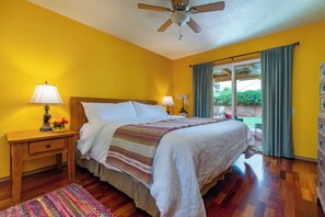 Habitación de hotel con cama de madera, dos lámparas de noche, ventilador de techo y vistas al exterior a través de una puerta corrediza de vidrio.