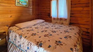 A wooden cabin room with a bed, a framed picture on the wall, and a window with curtains.