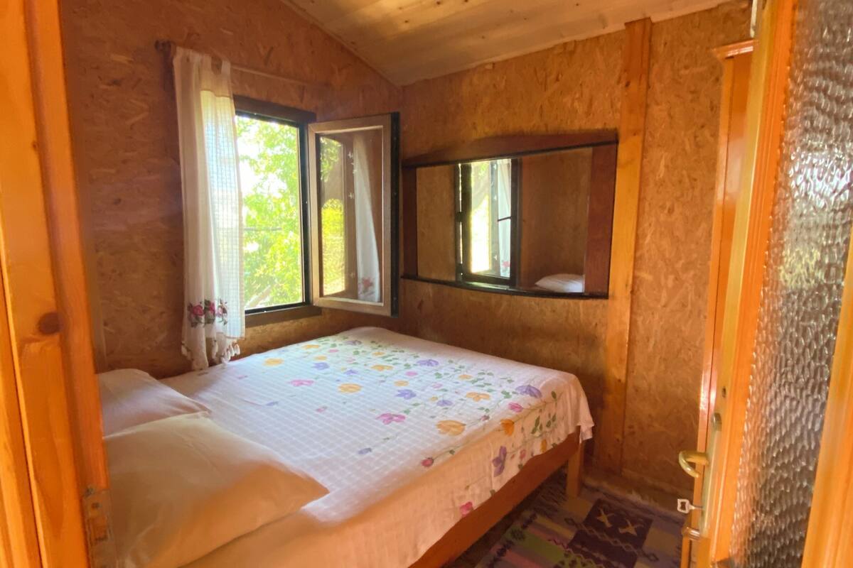Un dormitorio con techo de madera, una cama con colcha estampada, dos ventanas con cortinas y un espejo en la pared.