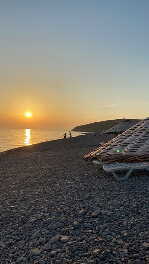 A pebbled beach with a sunset, a few people, and boats. - Aydeniz pansiyon (Karaburun)