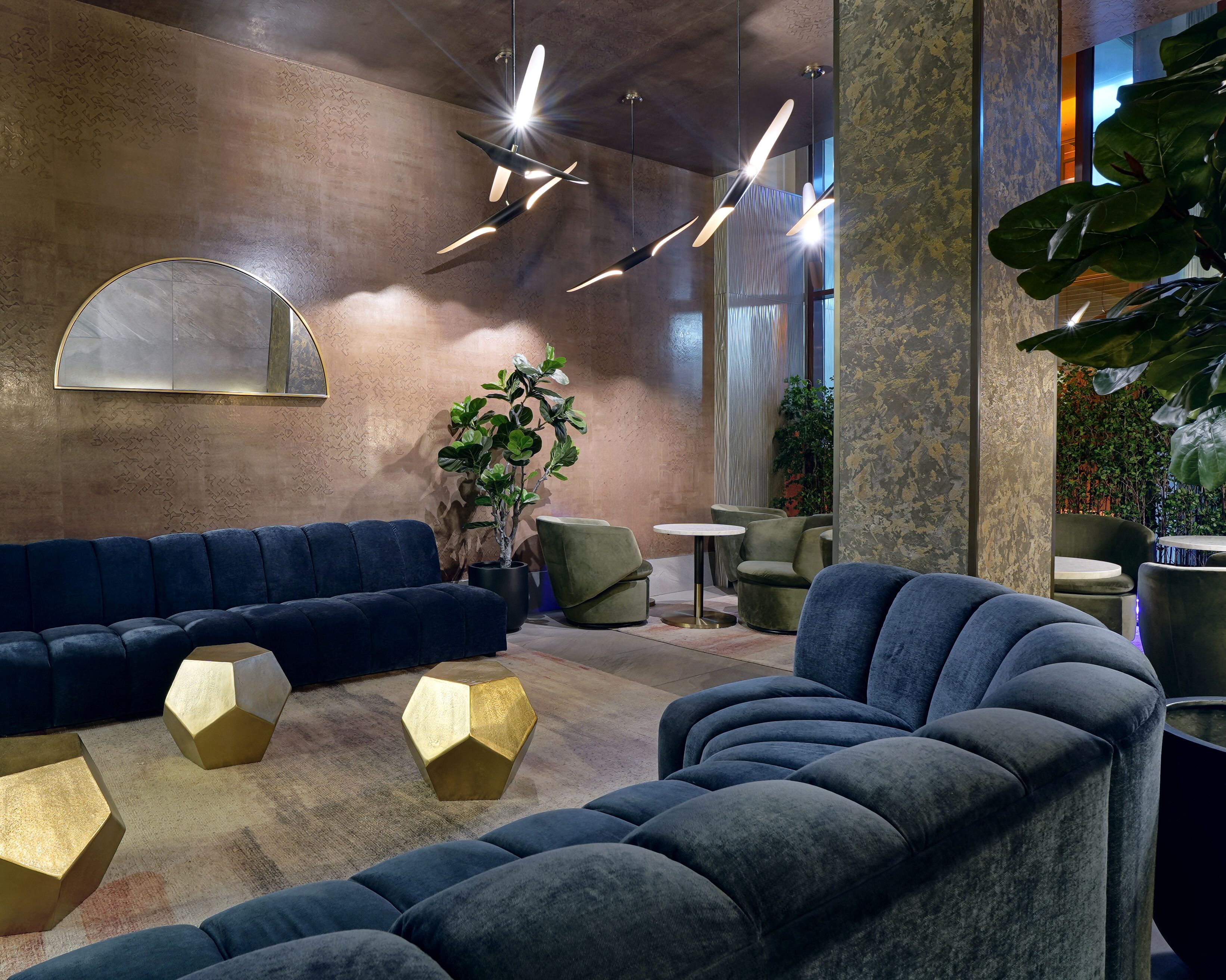 Un espace de détente moderne avec un canapé bleu, des tables d’appoint hexagonales dorées et des luminaires suspendus.