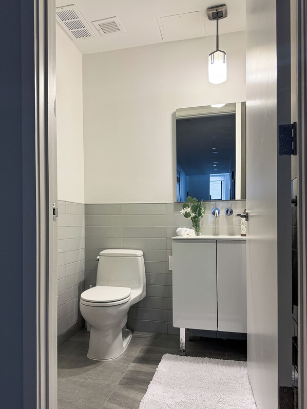 A modern bathroom with a toilet, sink, and mirror. - One Dutch Hotel (New York)