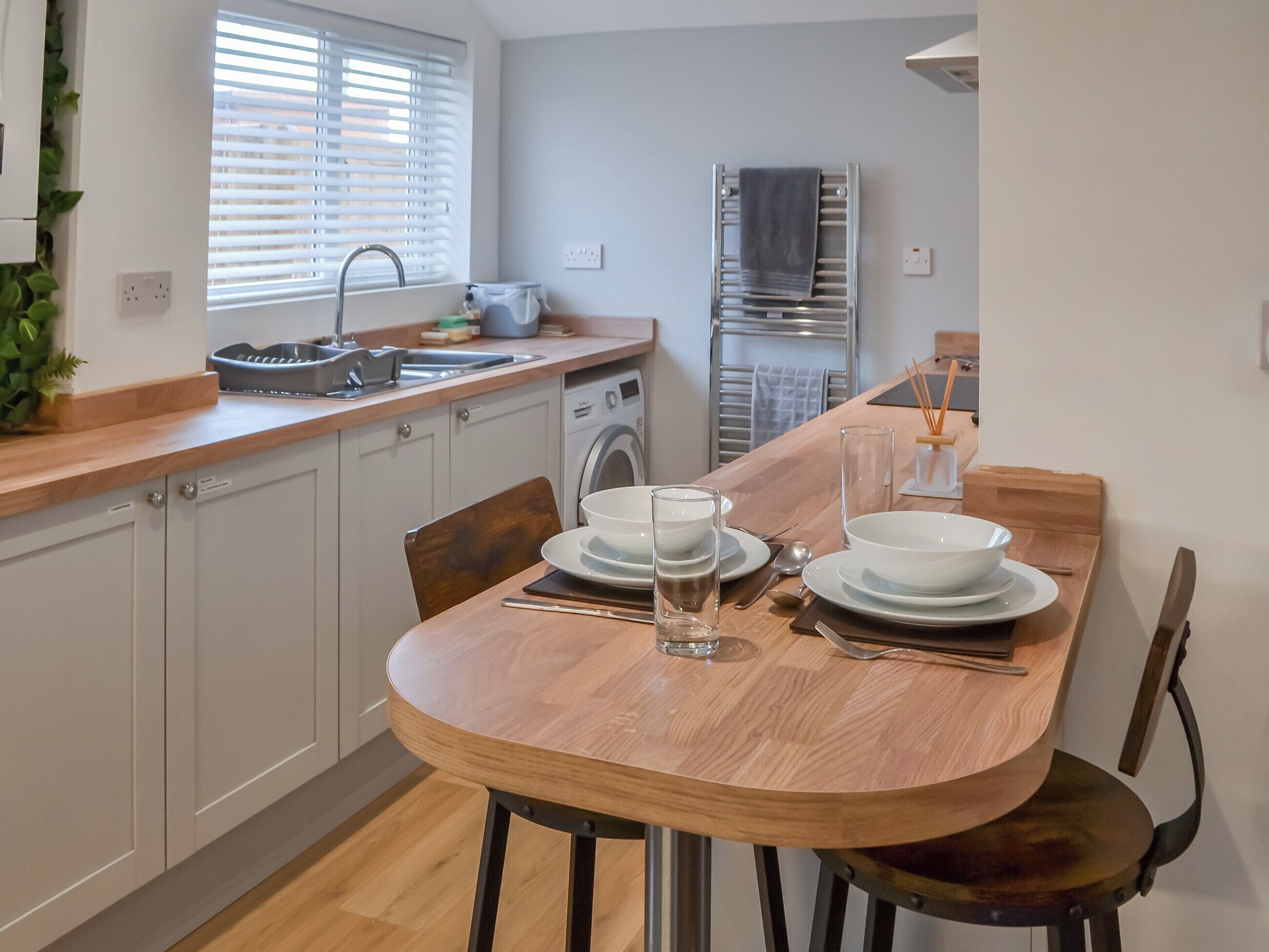 A modern kitchen with a dining table set for two, a washing machine, and a towel rack.