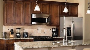 A kitchen with wooden cabinets, stainless steel appliances, granite countertops, and pendant lighting.
