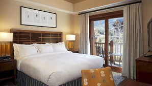 A hotel room with a large bed, two bedside lamps, a framed picture on the wall, and a view of a balcony with outdoor seating.