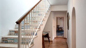 Una escalera con barandillas blancas y un pasamanos de madera que conduce a una habitación con piso de baldosas y una mesa de comedor con sillas.