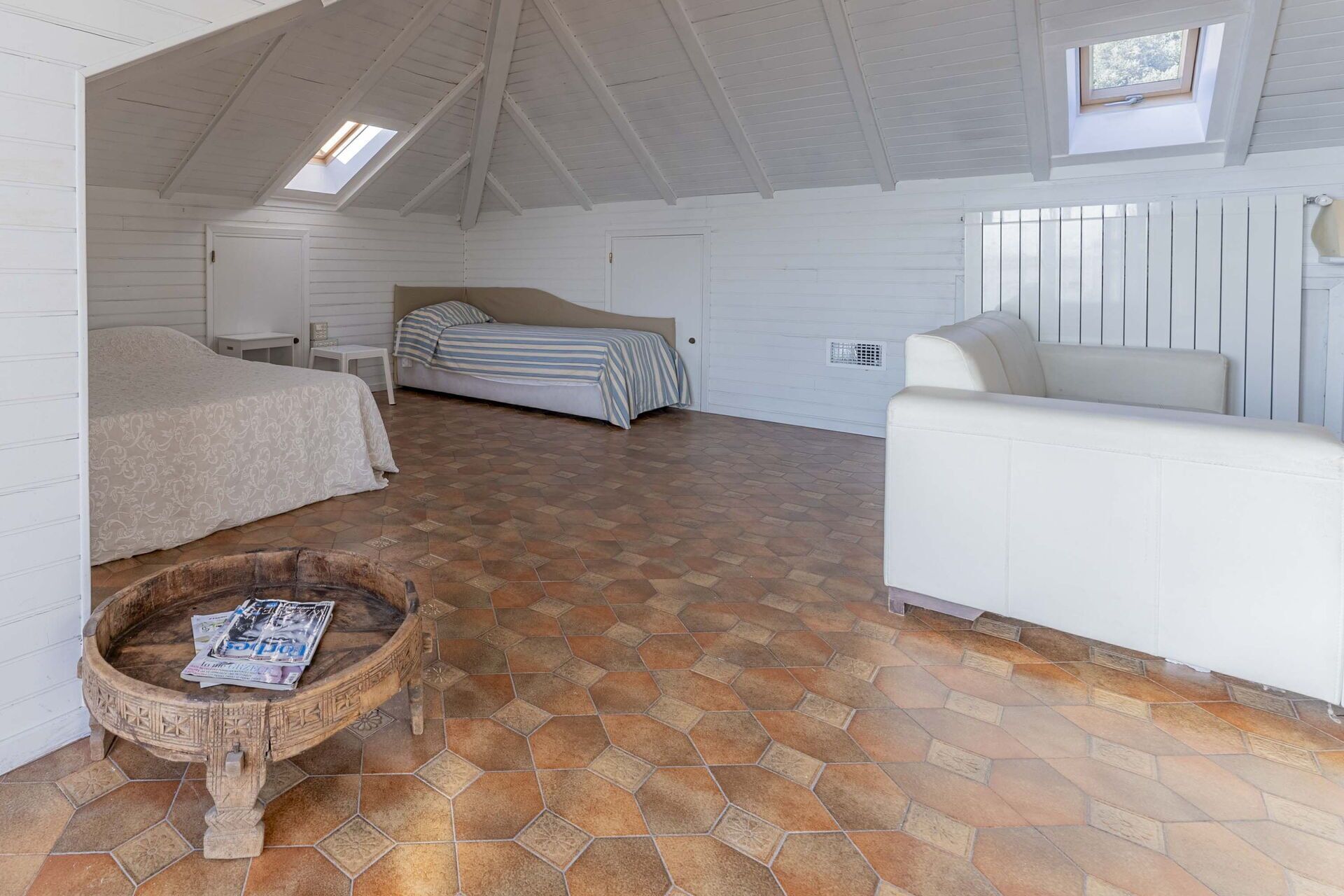 A bedroom with a bed, a sofa, a small table with newspapers, and a decorative basin.