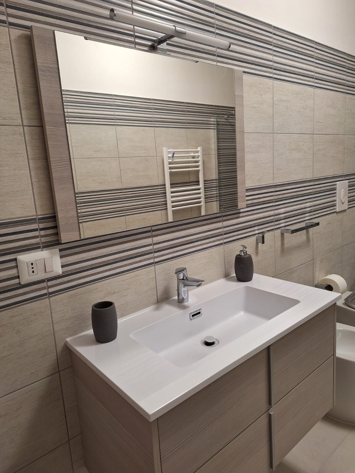 Un baño moderno con un espejo grande, dos lavamanos, un perchero para toallas y un inodoro.