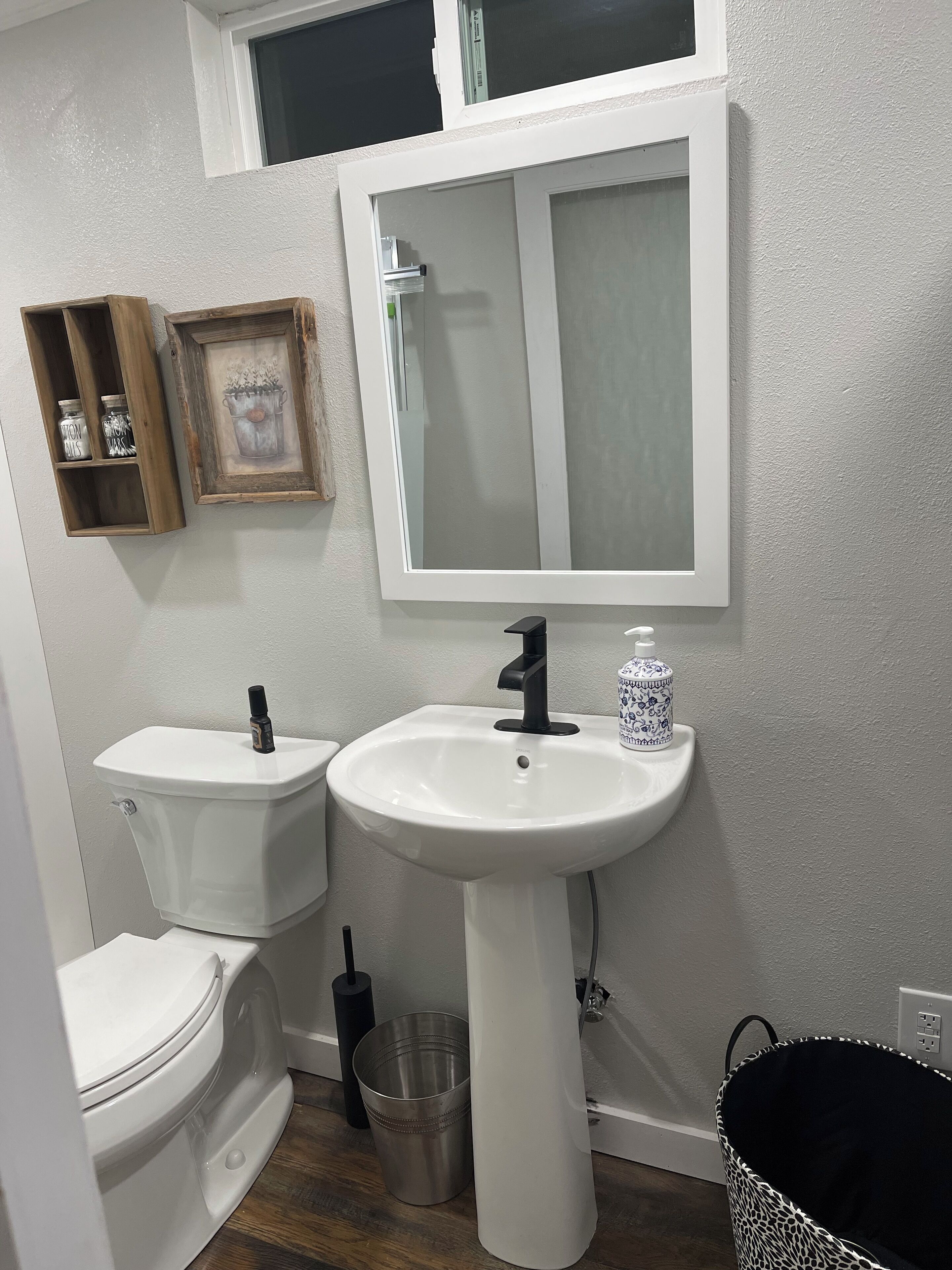 Une salle de bain avec des toilettes, un lavabo et une fenêtre située au-dessus du miroir.