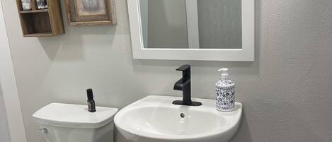 Une salle de bain avec des toilettes, un lavabo et une fenêtre située au-dessus du miroir.
