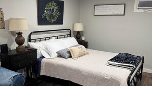Um quarto bem arrumado com uma cama, duas mesas de cabeceira com luminárias, um relógio de parede e um objeto decorativo na parede.