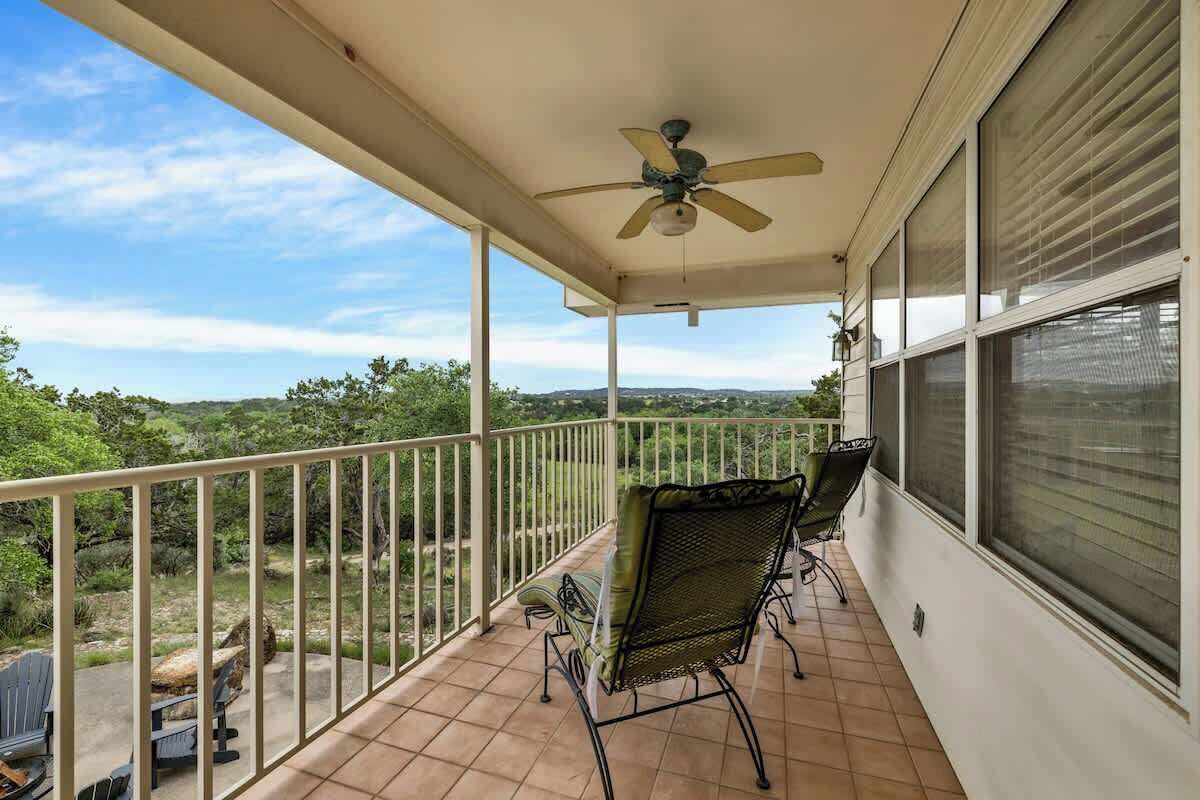 A covered balcony with a ceiling fan, a chair, and a view of the surrounding landscape.