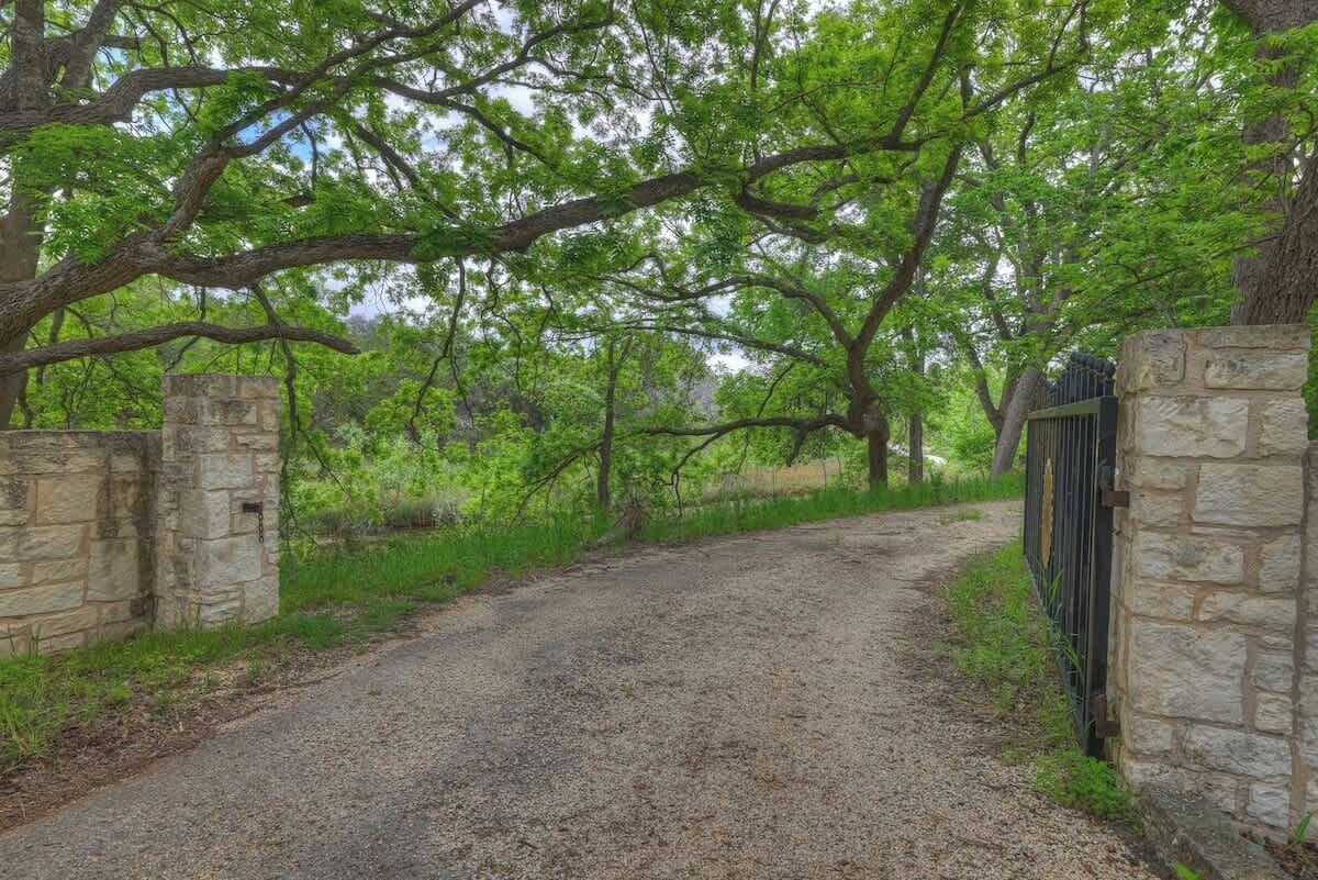 A gravel path flanked by stone walls and lush green trees.