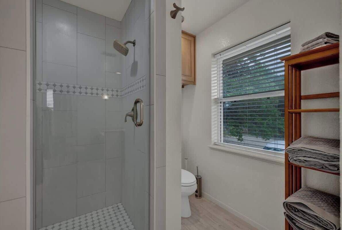 Ein Badezimmer mit Duschkabine aus Glas, Toilette und einem Fenster mit Jalousien.