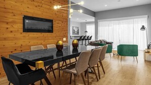 A modern dining area with a wooden wall, a black dining table, and multiple chairs. - Sunshine Escape! 5BR Disney-Area Villa with South-Facing Pool (Kissimmee)