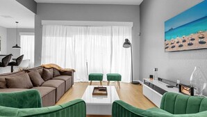 A modern living room with a sectional sofa, green armchairs, a coffee table, and a painting of a beach scene. - Sunshine Escape! 5BR Disney-Area Villa with South-Facing Pool (Kissimmee)