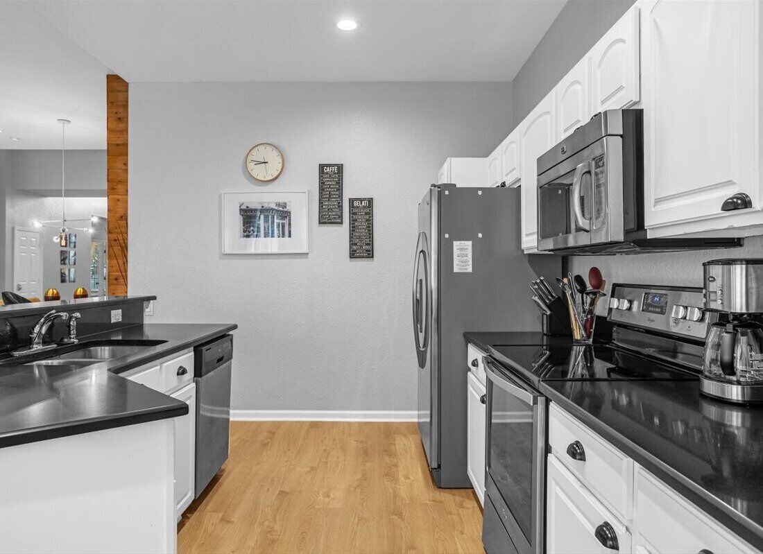 A modern kitchen with white cabinets, a stainless steel refrigerator, a microwave, and a coffee maker.