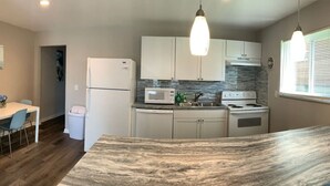 Una cocina moderna con armarios blancos, encimera de granito, microondas, estufa e iluminación colgante.
