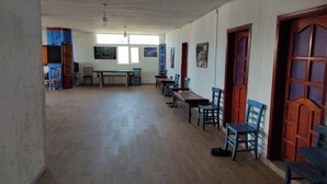 A spacious room with wooden flooring, several tables and chairs, and a large window providing natural light. - Dede Sebo Camping (Dogubayazit)